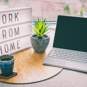 work from home sign, laptop, coffee and plant on a desk